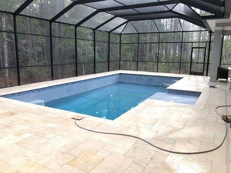 Screened-in backyard pool with blue water and beige tile patio