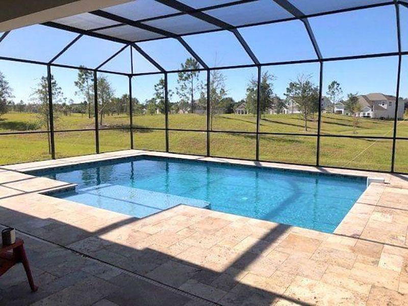 Screened-in backyard pool with blue water, stone deck, and grassy yard beyond.