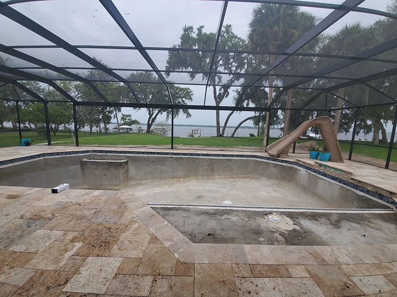 Empty outdoor swimming pool with cracked concrete and a covered canopy near water and trees