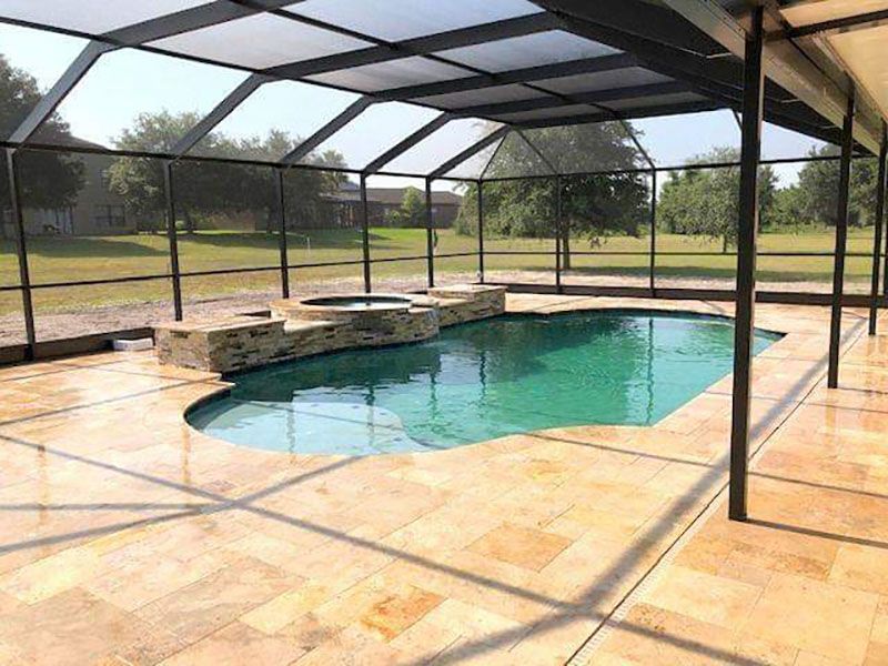Screened backyard pool with stone patio and covered lanai, showing turquoise water and lounge ledge.