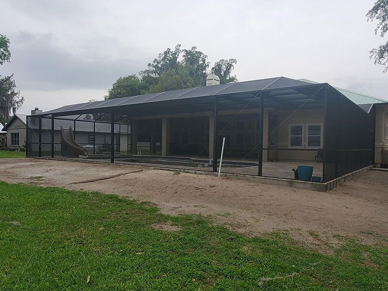 Large covered outdoor structure with a black roof and open sides on a dirt lot under cloudy skies
