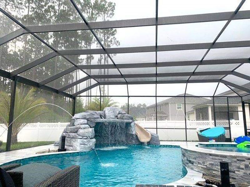 Screened-in backyard pool with rock waterfall and slide, turquoise water, and lounge chairs by the fence