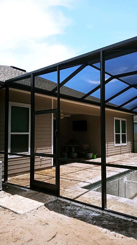 Backyard patio with a black-framed glass roof pergola beside a brick house and pool area