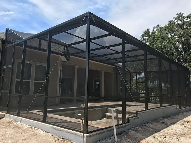 Black-framed screened patio enclosure beside a house, with concrete floor and trees in the background
