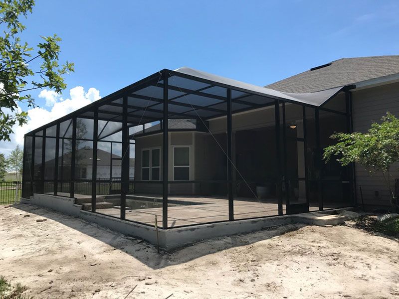 Black screened patio enclosure attached to a house on a dirt lot