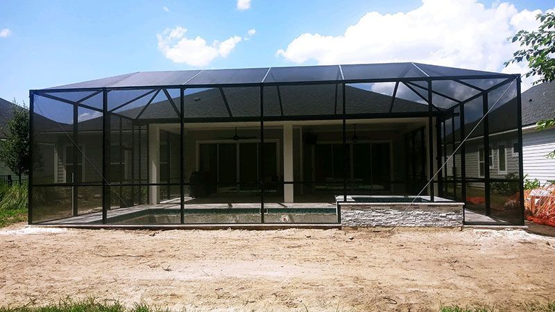 Black mesh-screened patio enclosure around a house with a concrete walkway and dirt foreground