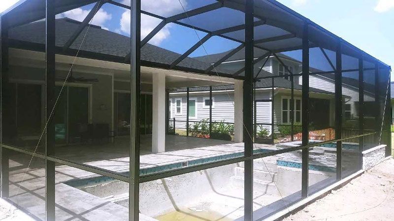 Black-framed glass patio enclosure with a slanted roof and paved floor, beside a building and pool.