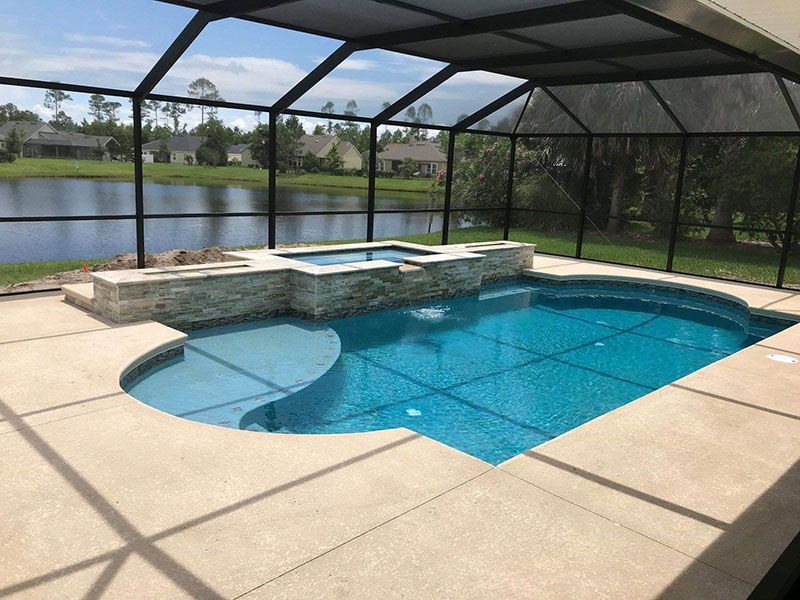 Screened backyard pool with tan patio, blue water, and lake view beyond the enclosure