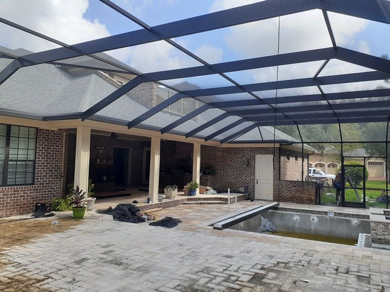 Covered patio with black pergola framing, brick house, and a small pool under construction in a backyard.