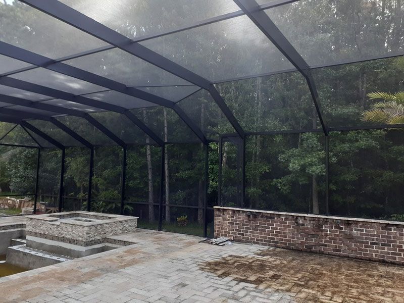 Screened-in patio with brick walls, stone seating, and wet floor overlooking dense trees