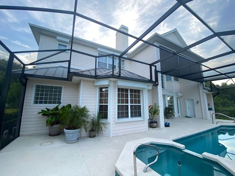 Back patio with screened enclosure, white two-story house, and turquoise swimming pool