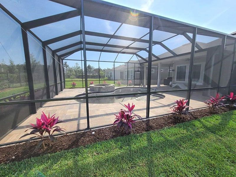 Screened backyard patio with a covered pool and pink plants along the edge