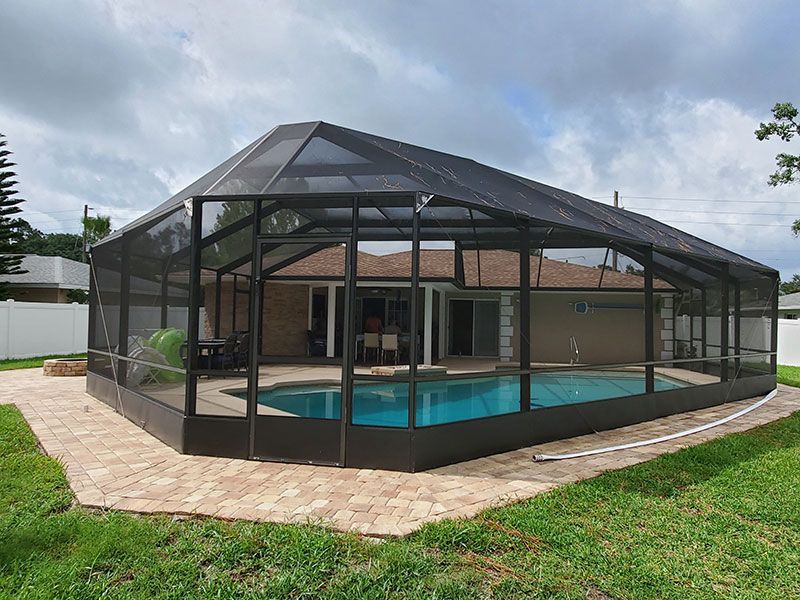 Screened pool enclosure around a backyard pool beside a tan house on a cloudy day