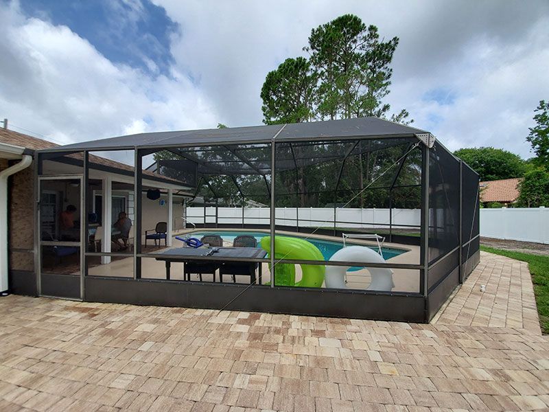 Screened outdoor patio with dining table, colorful chairs, and a poolside view.