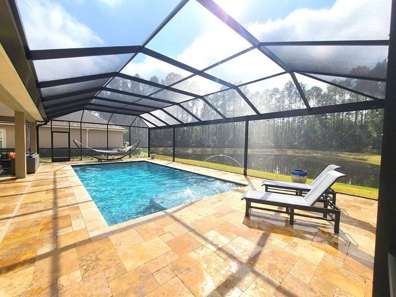 Screened-in pool with blue water, tan deck, and two lounge chairs in sunlight