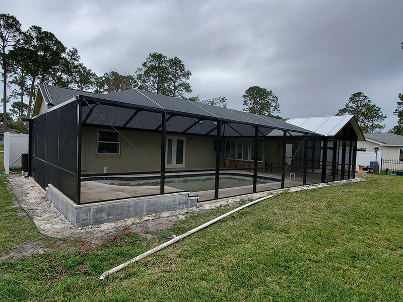 Single-story house with black screened porch and stone foundation on a grassy lot under cloudy skies