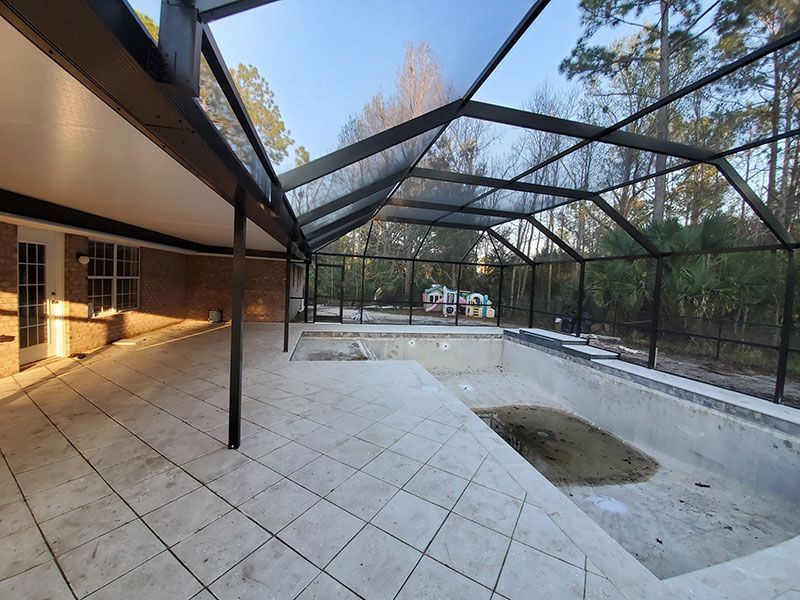 Empty screened-in patio with tiled floor, black frame, and an in-ground pool under construction