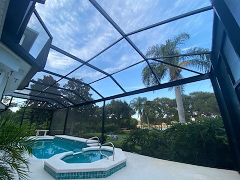 Screened pool and spa patio under blue sky, with palm trees and lush greenery beyond.
