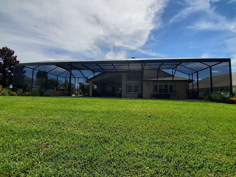 Single-story house with a large screened lanai behind a bright green lawn under a partly cloudy sky