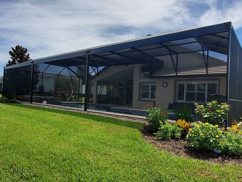 House with a large screened patio and green lawn, with flower beds in front