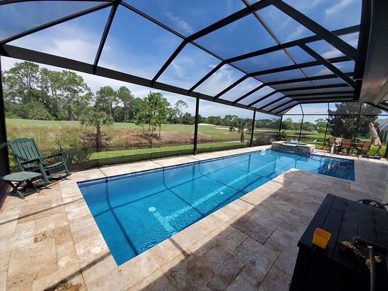 Screened-in backyard pool with blue water, stone deck, and lounge chairs overlooking a green lawn