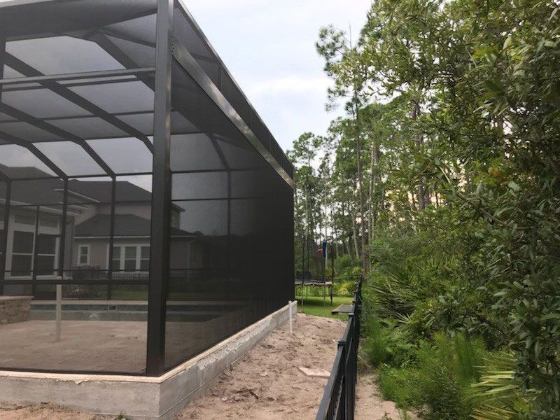 Screened patio beside a house, with a dirt path and trees along the right side.