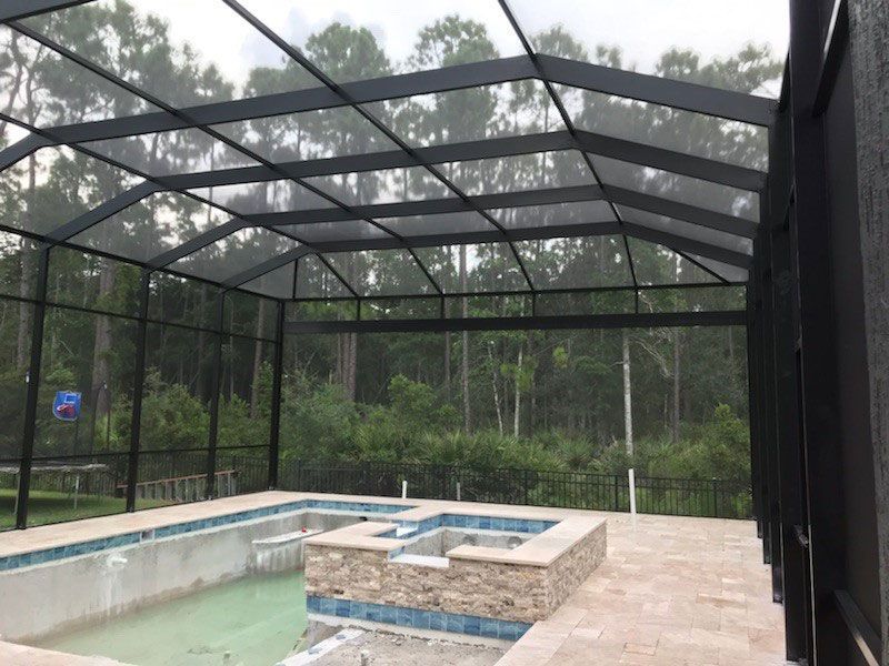 Screened-in backyard pool and spa with stone deck and black enclosure roof