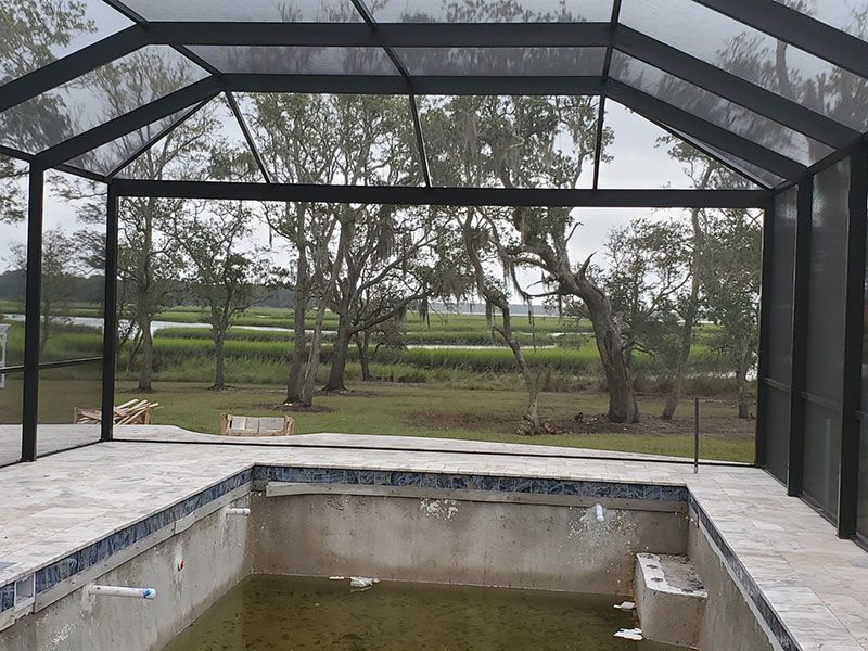 Screened patio with a partially filled rectangular pool overlooking a grassy yard and trees