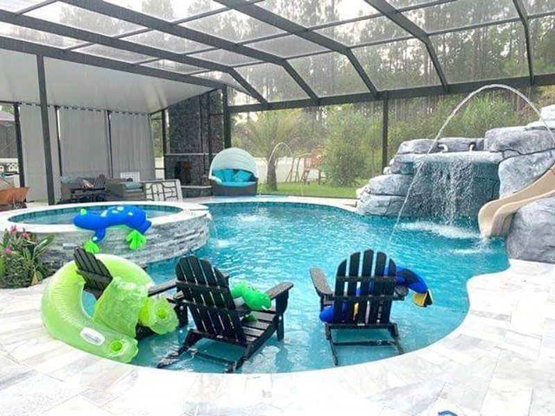 Backyard pool with screened enclosure, waterfall, two blue lounge chairs, and floating green and blue toys