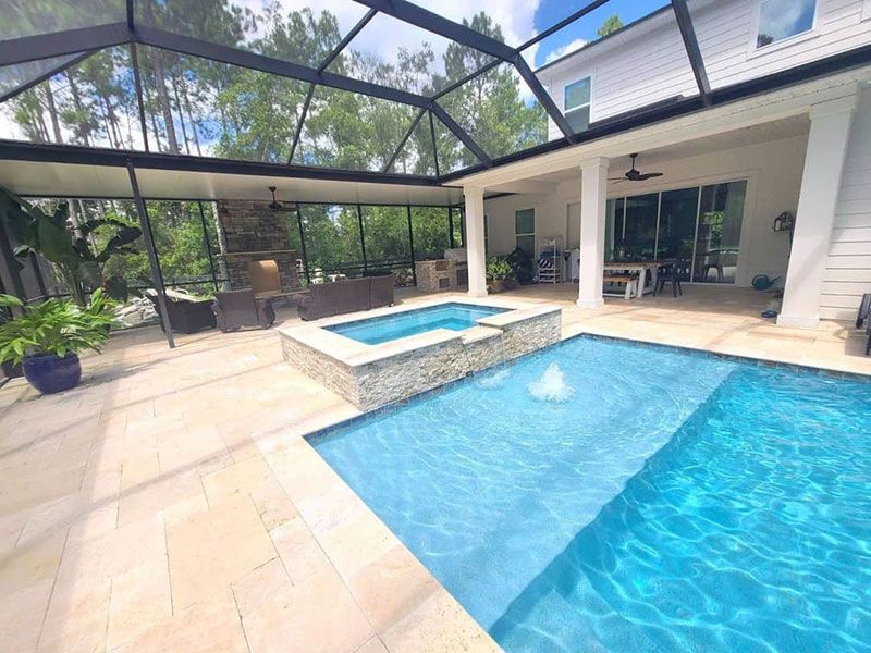 Modern backyard pool patio with hot tub, screened enclosure, and white house exterior