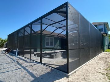 Black mesh-screened patio enclosure beside a house on a sunny day