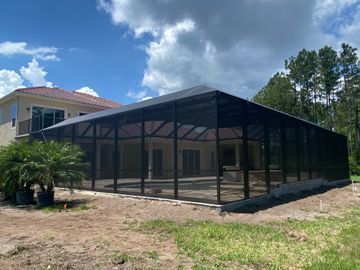 Black mesh screened enclosure beside a house under a cloudy blue sky