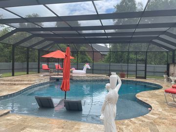 Screened-in backyard pool with red umbrella, lounge chairs, and swan float.