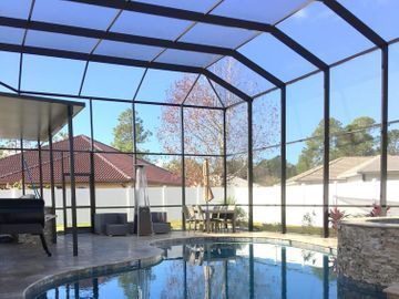 Screened backyard patio with a swimming pool, outdoor seating, grill, and stone bar area