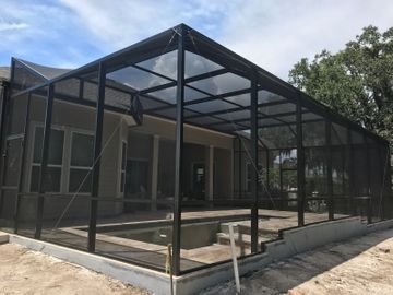 Screened patio enclosure with black metal frame beside a house and concrete walkway