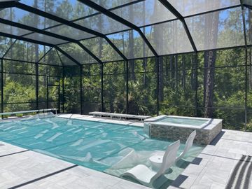 Screened-in backyard pool with lounge chairs and trees beyond the enclosure