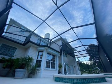 Backyard patio with screened enclosure, white house, and pool steps under a blue sky