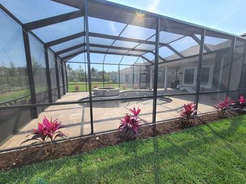 Screened pool enclosure with patio, central spa, and pink plants along the edge