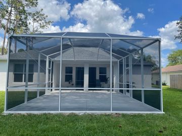 Backyard screened patio enclosure with white frame, concrete floor, and house behind it
