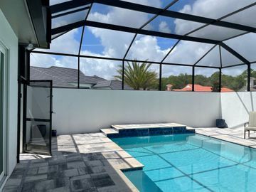 Screened backyard pool with blue water, white walls, and patio seating under a covered enclosure