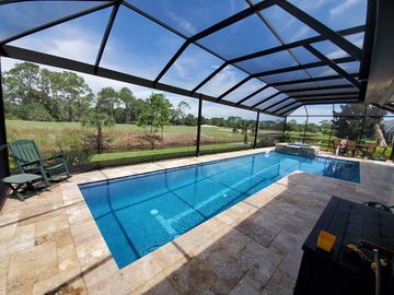 Covered backyard pool with blue water, lounge chairs, and a screened enclosure overlooking a grassy landscape