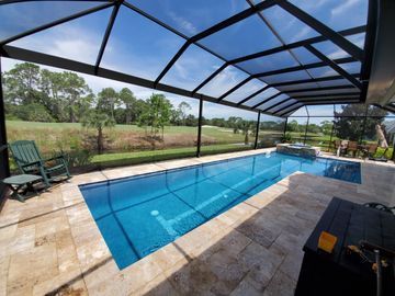 Indoor-outdoor pool with blue water under a screened patio, overlooking a grassy yard and trees