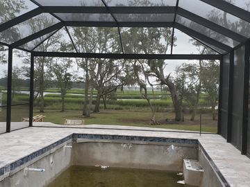 Screened pool enclosure with empty pool, tiled deck, and trees beyond the fence.