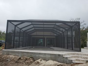 Black screened patio enclosure with a concrete base and steps under construction outdoors