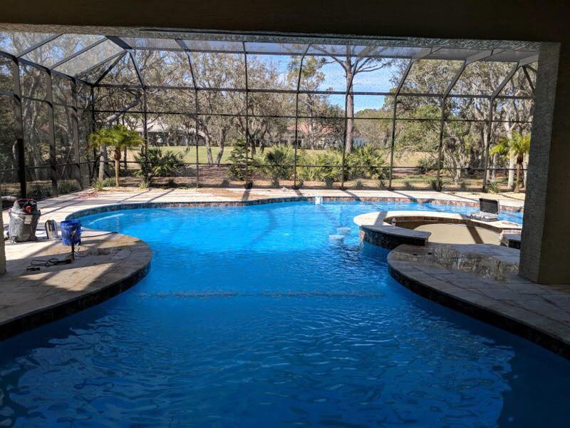 Outdoor resort pool with blue water and stone seating areas under a screened enclosure