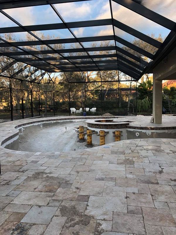 Outdoor patio with stone floor, curved seating, and a glass roof structure surrounded by trees at sunset