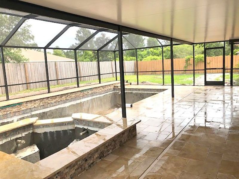 Screened patio with a built-in pool and wet tiled floor beside a fenced yard