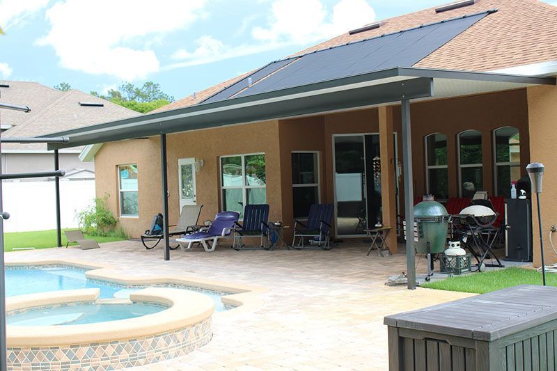 Backyard patio with covered seating area, pool, and grill beside a house