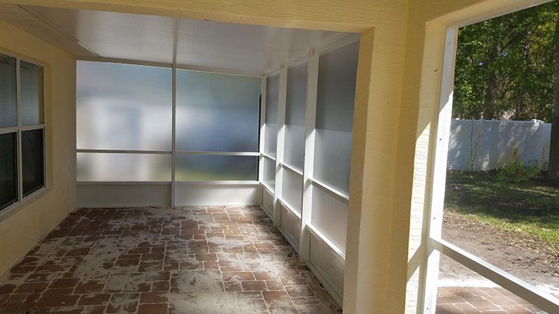 Empty sunroom with tiled floor, frosted windows, and open doorway to a grassy yard.