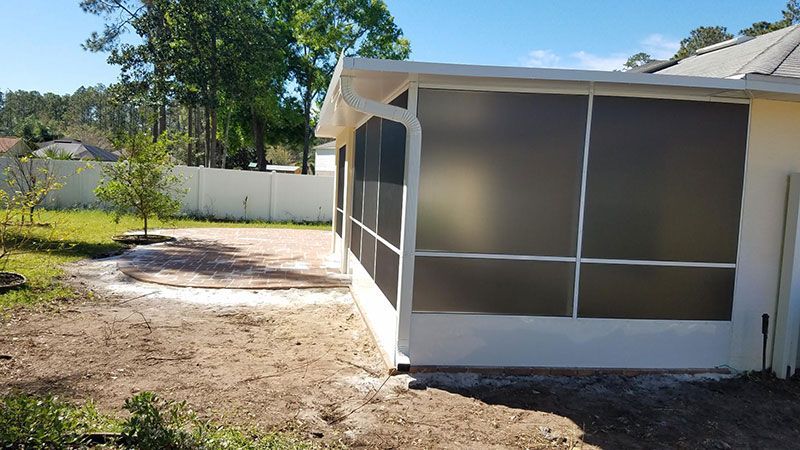 Screened porch attached to a white house in a sunny yard with dirt ground and trees nearby